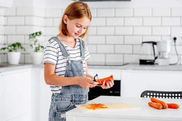 台所でニンジンを引く前の女の子と笑顔 家庭でのオレンジ野菜料理の子供 — ストック写真
