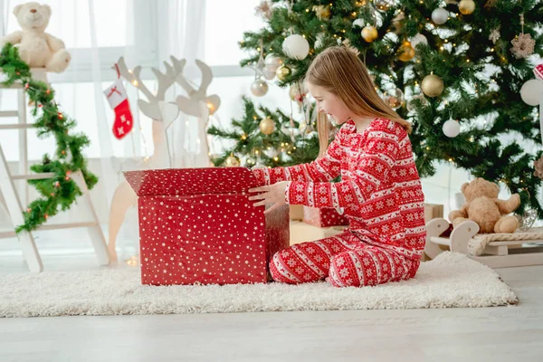 美しい子供の女の子は伝統的な装飾された木と家でクリスマスの赤いギフトボックスを開きます プレゼントで新年を祝う子供 — ストック写真