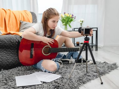 Gitar kaydı olan genç bir kız sosyal medyada blog takipçileri için kamerayla online ders veriyor. Genç müzisyen gitarist vlog çekiyor