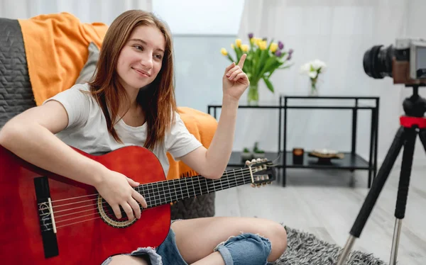 Girl teenager with guitar recording streaning online lesson with camera for blog followers in social media. Young musician guitarist filming vlog with tutorial at home