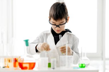 İlköğretim fen dersinde koruma gözlüğü takan öğrenci kimya deneyi yapıyor. Laboratuvarda kepek şişesi olan zeki bir öğrenci.