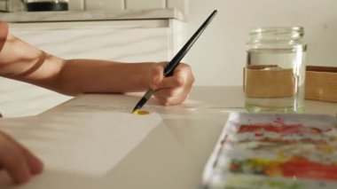 Çocuk eli boya fırçasını tutuyor ve kağıda suluboya boya ile çiziyor. Fırça ve akvaryumla resim yapan çocuk.