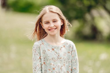 Küçük kız açık havada güneşli bir bahar gününde gülümsüyor. Doğada sevimli bir çocuk.