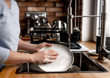 Girl washing plate dishes at kitchen at home with soap, foam and water. Woman cleaning utensil in sink
