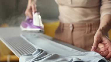 Girl hand using iron with steam mode for wrinkled clothes. Woman with hot electric tool smoothing textile