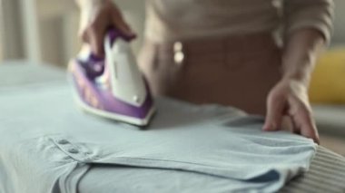 Girl hand using iron with steam mode for wrinkled clothes. Woman with hot electric tool smoothing textile on board