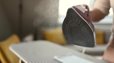 Girl hand using iron with steam mode for wrinkled clothes during housework. Woman with hot electric tool smoothing textile closeup