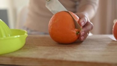 Girl cut ripe orange with knife for making natural juice at kitchen. Woman hand preparing tropical fruit drink