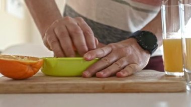 Man hand squeeze ripe orange with manual extractor for making natural juice at kitchen. Guy preparing tropical fruit drink