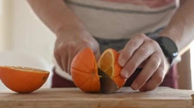 Man cut ripe orange with knife for making natural juice at kitchen. Guy hand preparing tropical fruit drink from citrus