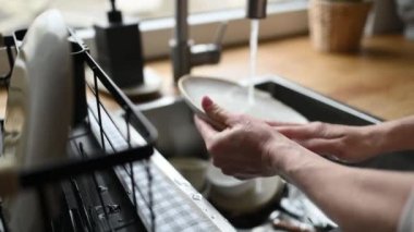 Girl washing plates and cups dishes at kitchen at home with soap, foam and water. Woman cleaning utensil and mugs in sink
