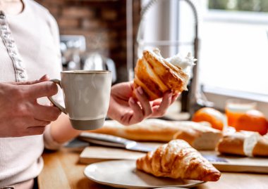 Girl holding cappuccino coffee mug and croissant at kitchen for french breakfast. Woman with pastry and espresso