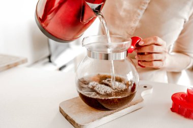 Girl pouring with hot tea from teapot cups at kitchen. Woman preparing warm herbal beverage with kettle and mugs