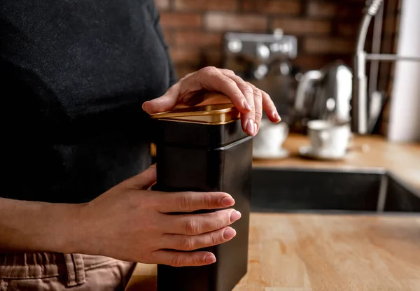 Girl opening tea black metal jar at kitchen to prepare hot natural beverage. Woman hands holding herbal drink container at home