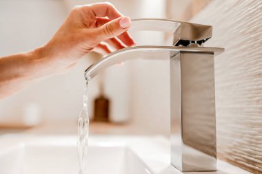 Girl hand open water from steel faucet in bathroom. Woman using silver tap at home for cleaning and hygiene