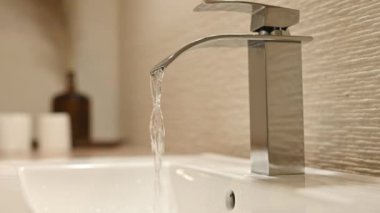 Girl hand closes running water from steel faucet in bathroom with environment care. Woman using silver tap at home