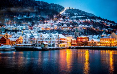 Bergen 'de ünlü Bryggen ticari malları, ahşap evleri ve kar mevsiminde ışıkları var. Noel zamanı tarihi liman binalarının manzarası denizlerde sihirli bir yansımayla