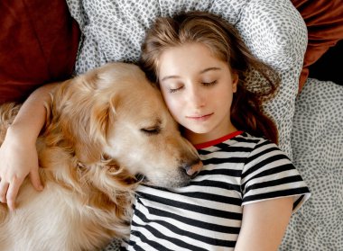 Pretty girl hugging golden retriever dog and sleeping in bed. Female teenager with purebred doggy pet labrador resting napping together