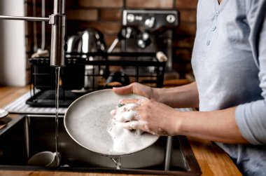 Girl washing plate dishes at kitchen at home with soap, foam and water. Woman cleaning utensil in sink