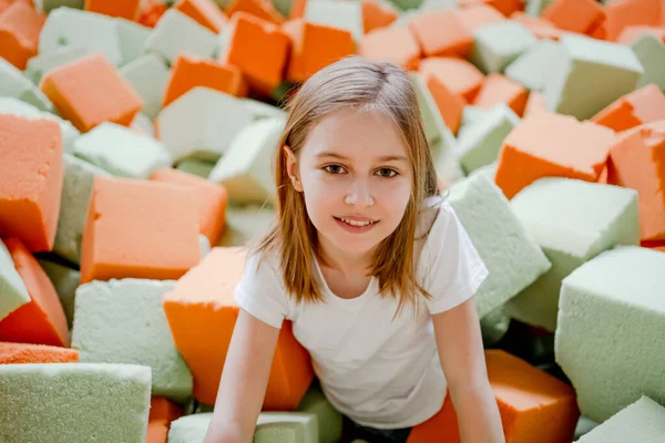 Pretty child girl in trampoline park having fun in colorful soft cubes and smiling. Cute preteen kid enjoying amusement activities