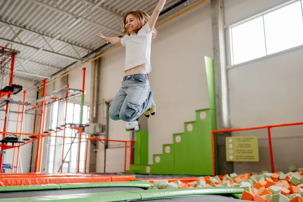 Pretty girl in trampoline park jumping with split and smiling. Happy little enjoying amusement activities