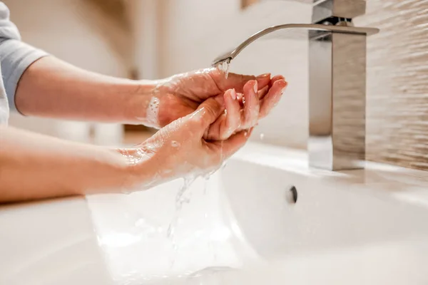 Girl washing hands with soap foam in bathroom with steel faucet. Hygiene and cleaning procedure to prevent virus and desease
