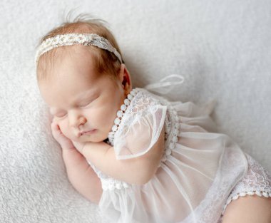 Newborn baby girl wearing wreath and tender dress sleeping holding tiny hands under her cheek. Infant child kid napping studio portrait