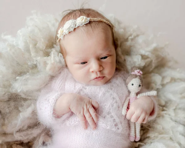 花輪を着た新生児の女の子は毛皮の上に横たわっており ニットのプリンセス人形を保持しています 幼児子供とともにおもちゃスタジオ肖像画 — ストック写真