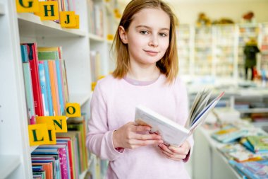 Okul kütüphanesinde kitap seçen liseli kız. Okumak için edebiyat seçen zeki bir kız. Kitapçıdaki raflardaki kitaplar. Kitaplardan öğreniyorum. Okul eğitimi. Günlük okumanın faydaları