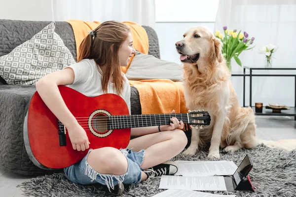 十几岁的女孩坐在地板上练习与金毛猎犬一起弹奏吉他 漂亮的吉他手 带着乐器 带着纯正的宠物狗 看着相机 — 图库照片