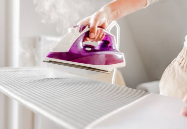 Girl hand holding iron with steam mode closeup. Woman with hot electric tool for smoothing textile and wrinkled clothes