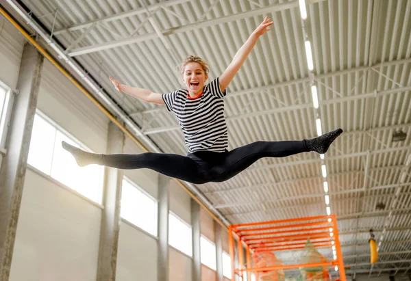 Pretty girl in trampoline park jumping and making split pose in air. Happy teenager enjoying amusement activities and stretching