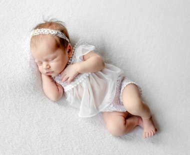 Newborn baby girl wearing wreath and tender dress sleeping holding tiny hands under her cheek. Infant child kid napping studio portrait