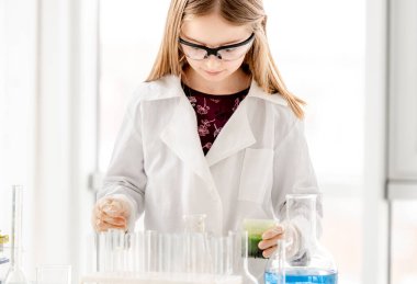 Korunma gözlüğü takan bir kız bilimsel kimya deneyi yapıyor. Okul dersinde teçhizatlı ve kimyasal sıvılı liseli kız.