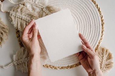 Girl hands holding watercolor paper postcard blank on boho decor background. Artist with aquarelle empty card in minimal natural design arrangment with copy space