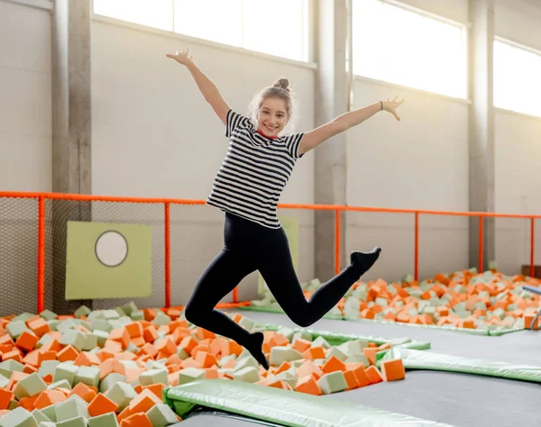Pretty girl in trampoline park jumping and posing in motion. Happy teenager enjoying amusement activities