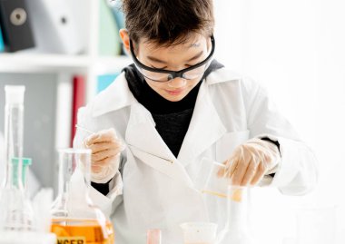 İlköğretim fen dersinde kimya deneyi yapan, kirli yüzlü, koruyucu gözlüklü bir öğrenci. Laboratuvarda zeki bir öğrenci.