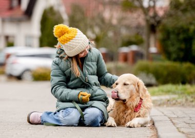 Sonbahar sokağında asfalt üzerinde Golden Retriever köpeğiyle oturan genç kız şapkası ve kalın ceketi vardı. Saf kan evcil köpek labrador 'unu seven güzel bir çocuk.