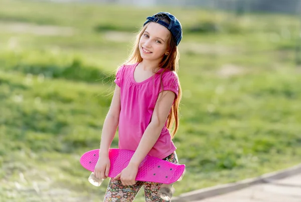 魅力的な十代の少女の保有物の彼女の明るいピンク スケート ボード キャップ笑顔 — ストック写真