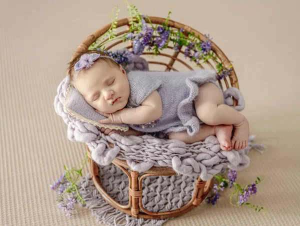 刚出生的女婴穿着针织衣服 头戴花环睡在用紫色花朵装饰的椅子上 可爱的幼儿小睡 — 图库照片