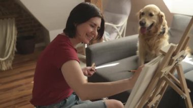 Güzel kız ressam Golden retriever köpeğiyle çizim yapıyor. Kalem ve tuval kullanarak. Güzel genç bir kadın, sevimli bir köpeğin portresini çiziyor.