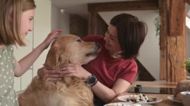 Altın av köpeği olan anne ve kızı kahvaltıyı hazırlıyor ve gülümsüyor. Safkan köpekli genç bir kadın ve kız ailesi kremalı süt yiyor.