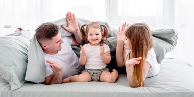 Battaniyenin altında el ele tutuşup gülümseyen güzel bir aile. Küçük kızıyla oynaşan genç ebeveynler.