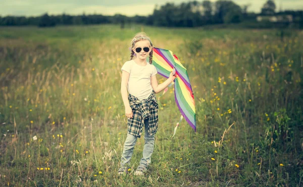 可爱的小女孩摆在一块草地上放风筝了阳光明媚的日子 — 图库照片