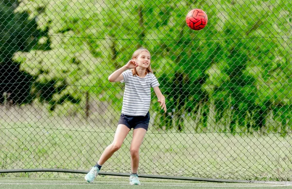 Pretty child girl catching football ball defending goal. Cute female kid at socker field playing