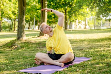 Yazın dışarıda minderde yoga yapan bir adam. Adam kaslarını germek için pilates yapıyor.