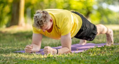 Kalas pozisyonunda duran ve yazın dışarıda yoga yapan bir adam. Kaslarını germek ve kaslarını germek için pilates yapan adam.