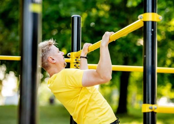 男人在公园外面用水平酒吧拉车是为了健康的生活 运动员为锻炼肌肉和健美做了大量的运动 — 图库照片