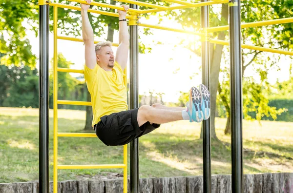 男子做腹肌运动与水平酒吧在公园外为了健康的福祉 运动员的腹部肌肉有很强的运动能力 — 图库照片