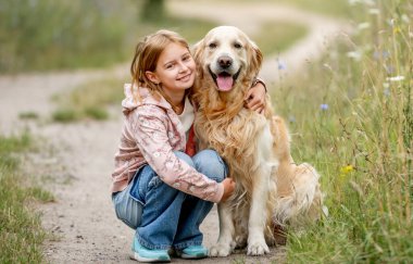Golden Retriever köpeği olan genç bir kız doğaya bakar ve arkasına bakar. Tatlı çocuk yazın parkta safkan köpeğe sarılıyor.